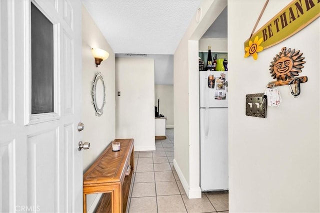 hall featuring a textured ceiling, baseboards, and light tile patterned flooring