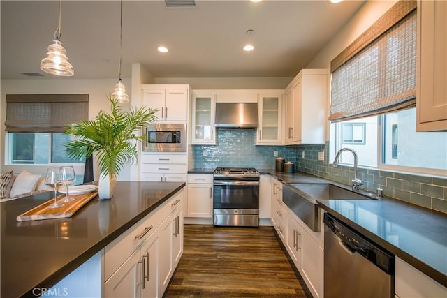 kitchen with a sink, dark countertops, stainless steel appliances, range hood, and white cabinetry