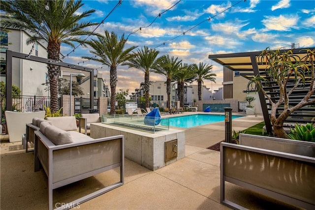 pool at dusk with fence, a patio, an outdoor living space, and a community pool