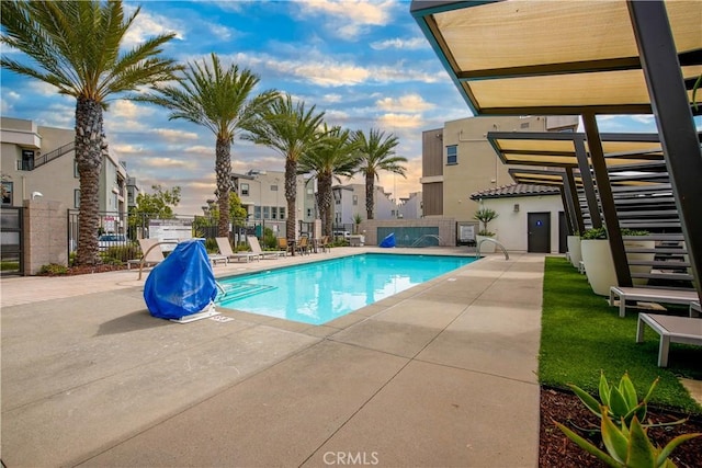 pool at dusk with a patio area, fence, and a community pool