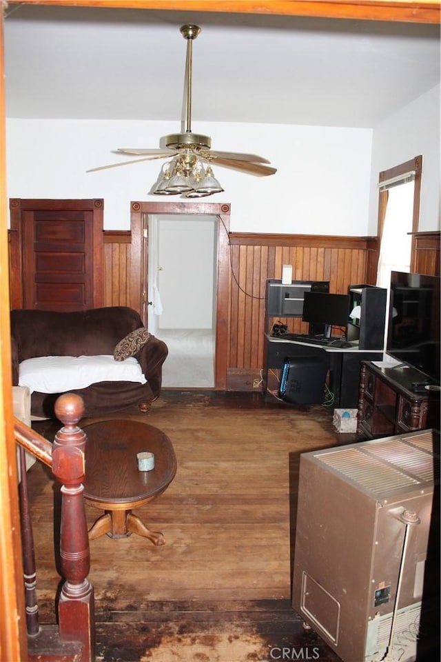 living area featuring wainscoting, ceiling fan, wooden walls, and dark wood-type flooring