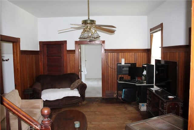 living area with wooden walls, a wainscoted wall, a ceiling fan, and wood finished floors