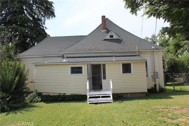 rear view of house with a lawn, a chimney, a shingled roof, and fence