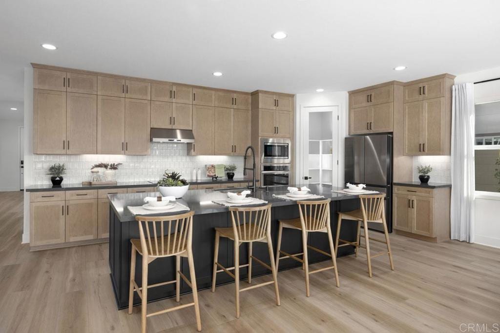 kitchen featuring dark countertops, stainless steel appliances, light brown cabinetry, and under cabinet range hood