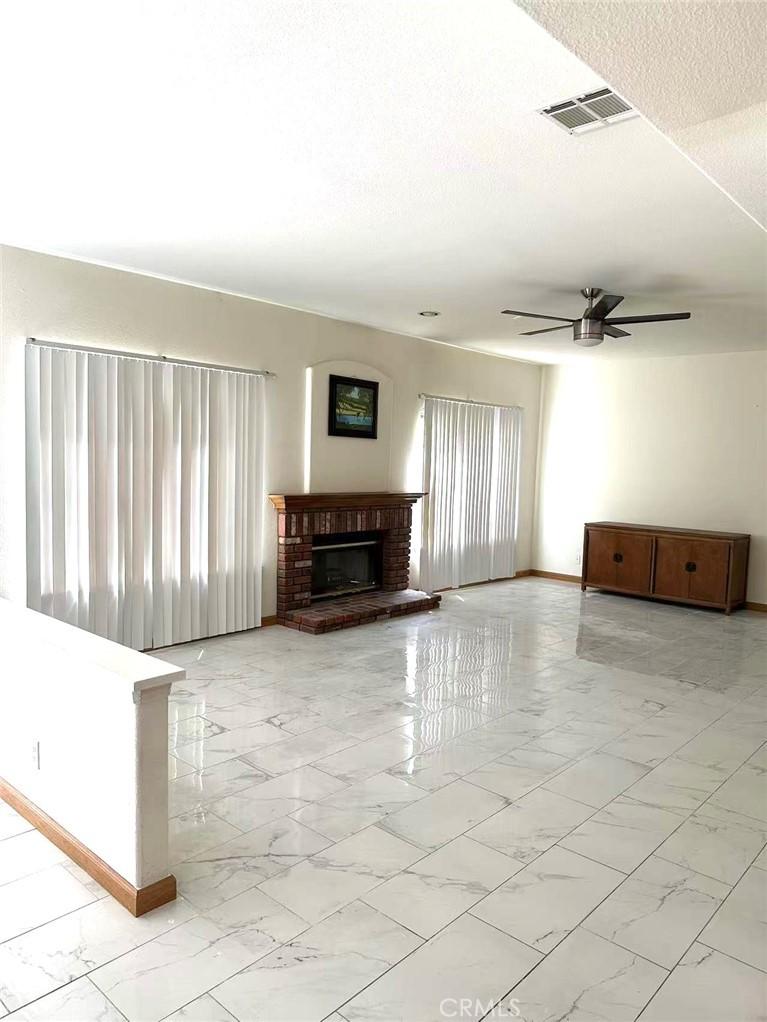 unfurnished living room featuring a ceiling fan, baseboards, marble finish floor, visible vents, and a brick fireplace