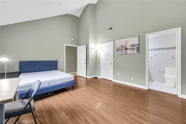 bedroom featuring wood finished floors, high vaulted ceiling, visible vents, connected bathroom, and baseboards