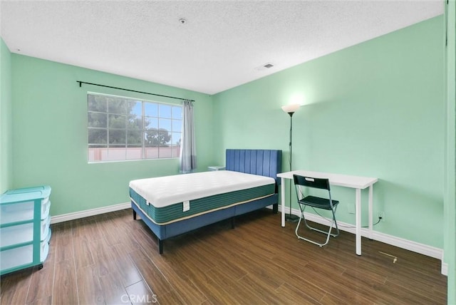bedroom featuring a textured ceiling, baseboards, visible vents, and wood finished floors