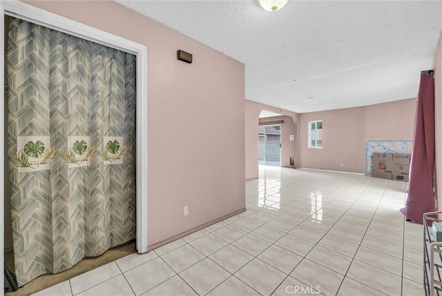 unfurnished room with arched walkways, baseboards, light tile patterned floors, and a textured ceiling