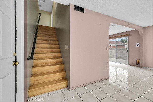 staircase featuring arched walkways, tile patterned flooring, and visible vents