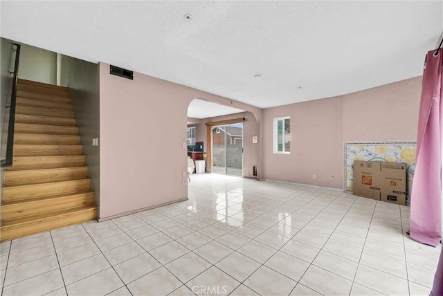 unfurnished living room featuring stairs, arched walkways, light tile patterned floors, and visible vents