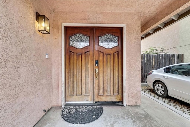 view of exterior entry featuring stucco siding and fence