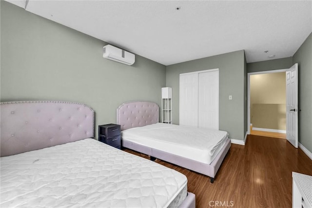 bedroom with baseboards, a closet, a wall unit AC, and wood finished floors