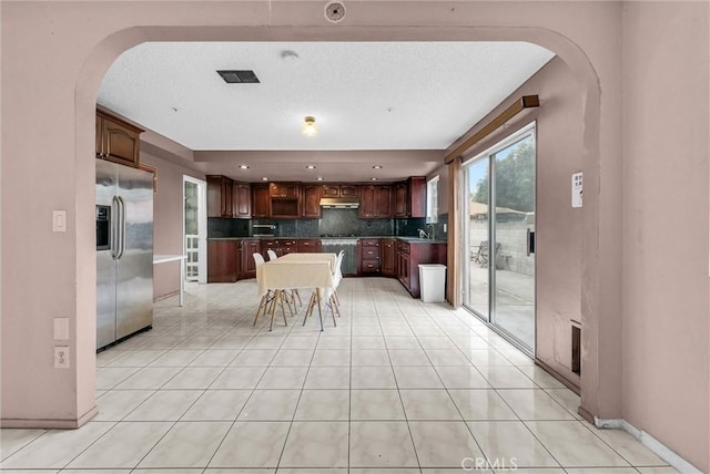 kitchen with under cabinet range hood, a sink, stainless steel fridge, arched walkways, and backsplash