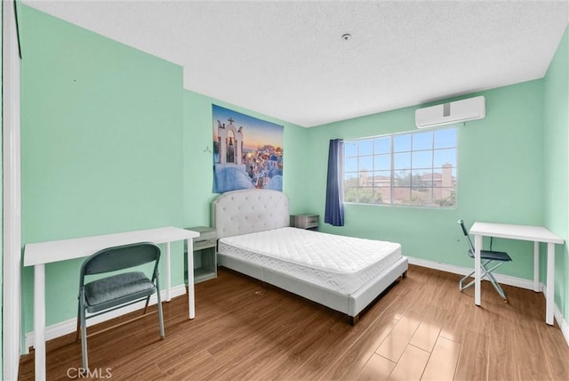 bedroom with a textured ceiling, wood finished floors, baseboards, and a wall unit AC