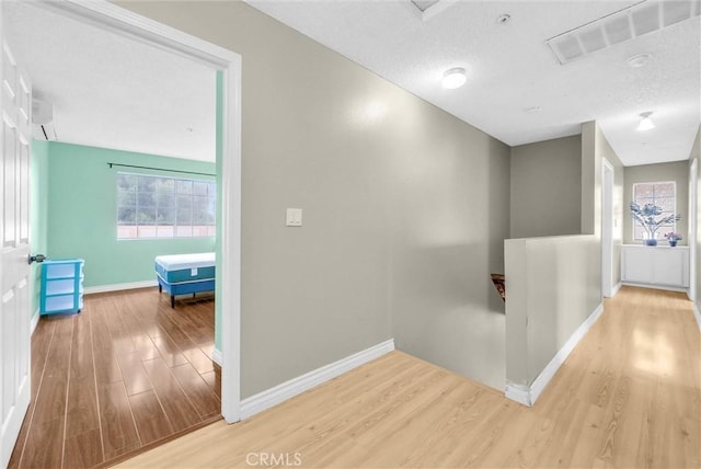 corridor featuring a textured ceiling, baseboards, visible vents, wood finished floors, and an upstairs landing