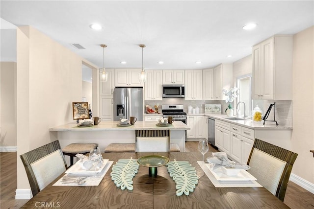 kitchen featuring a sink, a peninsula, visible vents, light wood-style flooring, and appliances with stainless steel finishes