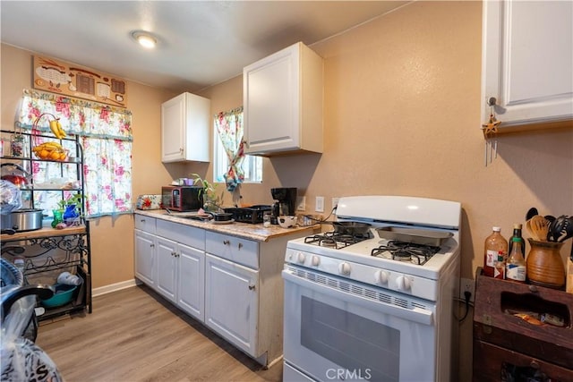 113 E White St, Barstow, CA 92311 - kitchen featuring white gas stove, light countertops, white cabinetry, light wood-type flooring, and black microwave