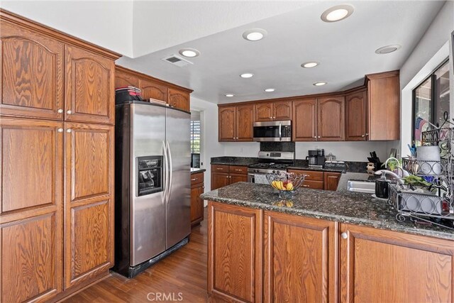 2757 Cape Dr, Corona, CA 92882 - kitchen featuring stainless steel appliances, dark wood finished floors, dark stone countertops, a peninsula, and brown cabinetry