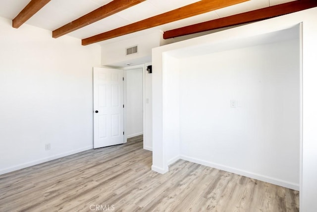 spare room featuring baseboards, beam ceiling, light wood-style flooring, and visible vents
