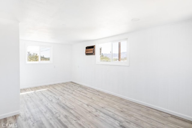empty room with a wealth of natural light, light wood-style floors, and baseboards