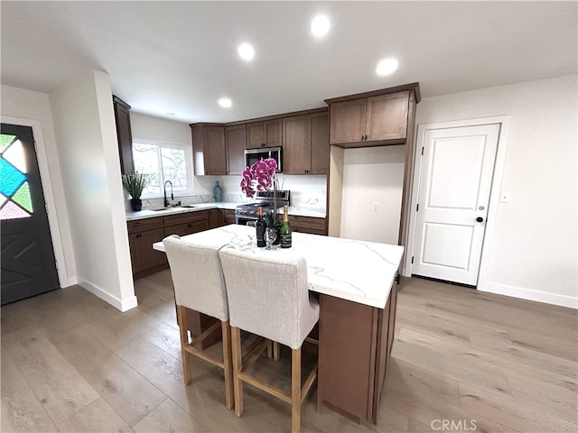 kitchen with stainless steel appliances, a sink, baseboards, light wood-style flooring, and recessed lighting