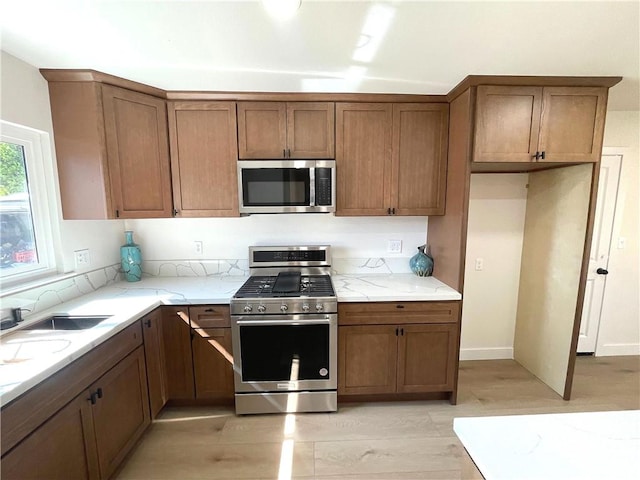 kitchen featuring appliances with stainless steel finishes, light stone counters, brown cabinetry, and a sink