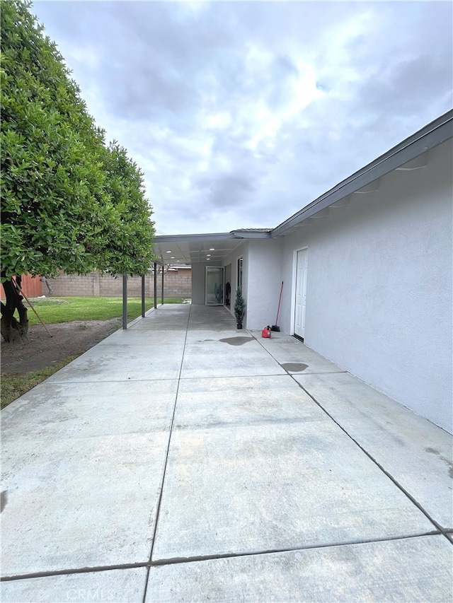 view of patio / terrace featuring concrete driveway, fence, and an attached carport