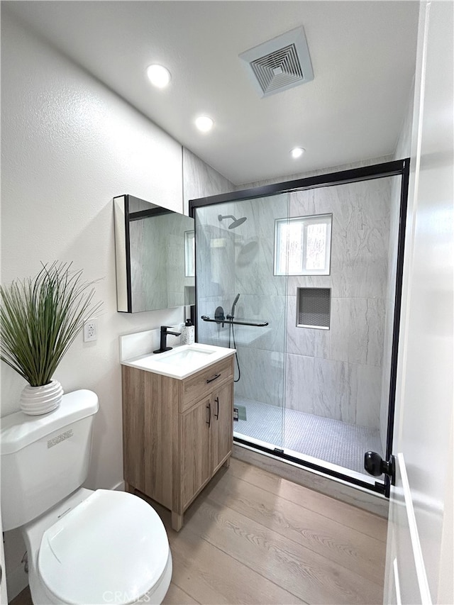 bathroom featuring wood finished floors, vanity, a shower stall, toilet, and recessed lighting