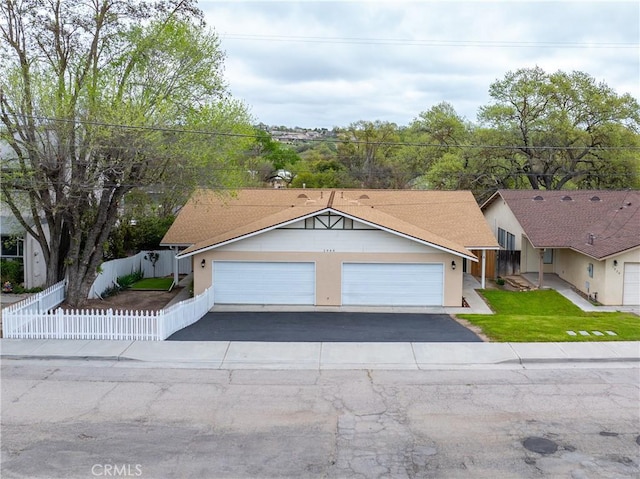ranch-style house with driveway, a garage, stucco siding, fence private yard, and a front lawn