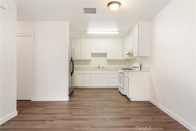 kitchen featuring freestanding refrigerator, baseboards, a sink, white gas stove, and light countertops
