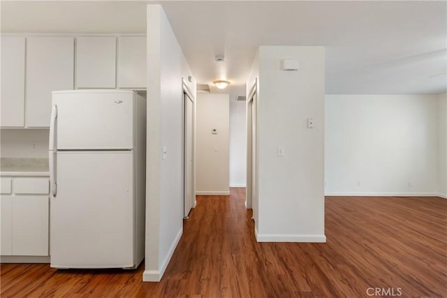 kitchen with freestanding refrigerator, white cabinetry, baseboards, and wood finished floors