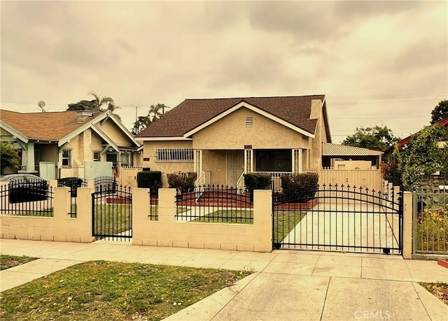 bungalow-style house featuring a gate, a shingled roof, stucco siding, and a fenced front yard
