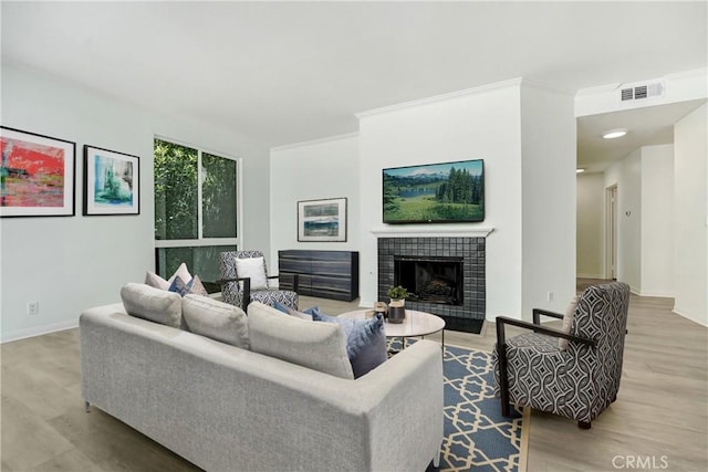 living area with wood finished floors, a tiled fireplace, crown molding, visible vents, and baseboards