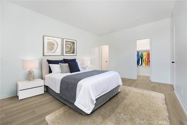 bedroom featuring a closet, light wood-type flooring, baseboards, and a spacious closet