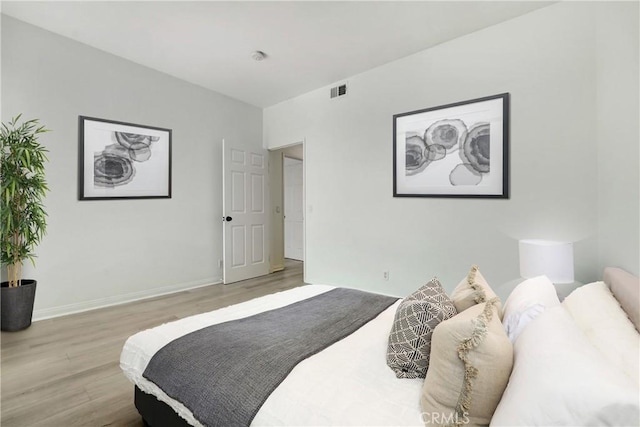 bedroom with baseboards, visible vents, and wood finished floors