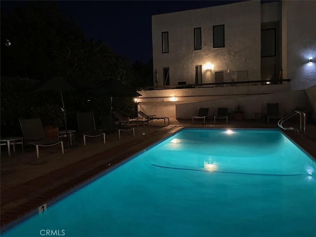pool at night featuring a patio area and a community pool