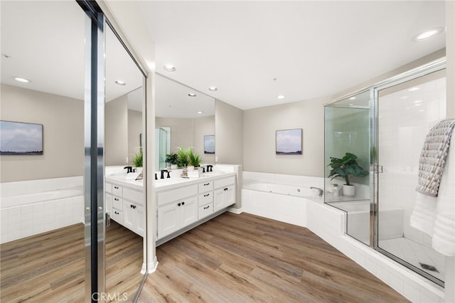 bathroom featuring a shower stall, double vanity, a bath, and wood finished floors