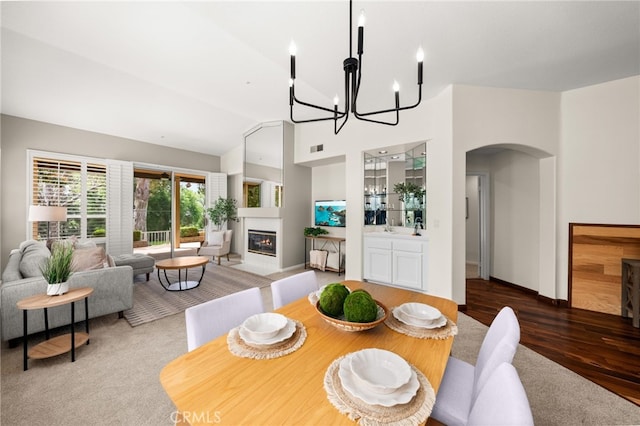 dining space featuring wood finished floors, a fireplace with flush hearth, visible vents, arched walkways, and a chandelier