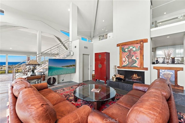 living room featuring stairway, a high ceiling, a warm lit fireplace, and visible vents
