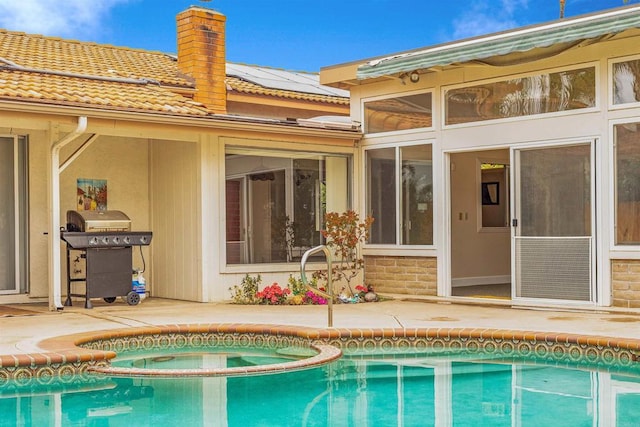 back of house with a chimney, a patio, an outdoor pool, solar panels, and an in ground hot tub