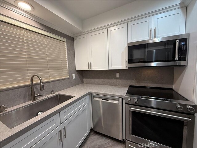 kitchen featuring a sink, white cabinetry, backsplash, light countertops, and appliances with stainless steel finishes