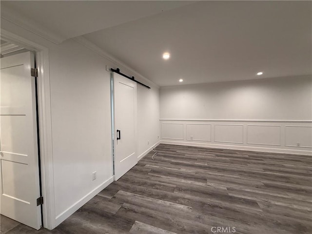 basement featuring dark wood-style flooring, a barn door, baseboards, and recessed lighting