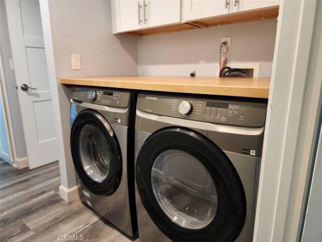 clothes washing area with washing machine and clothes dryer, baseboards, cabinet space, and wood finished floors