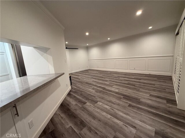 finished below grade area with recessed lighting, a barn door, ornamental molding, dark wood finished floors, and a wainscoted wall