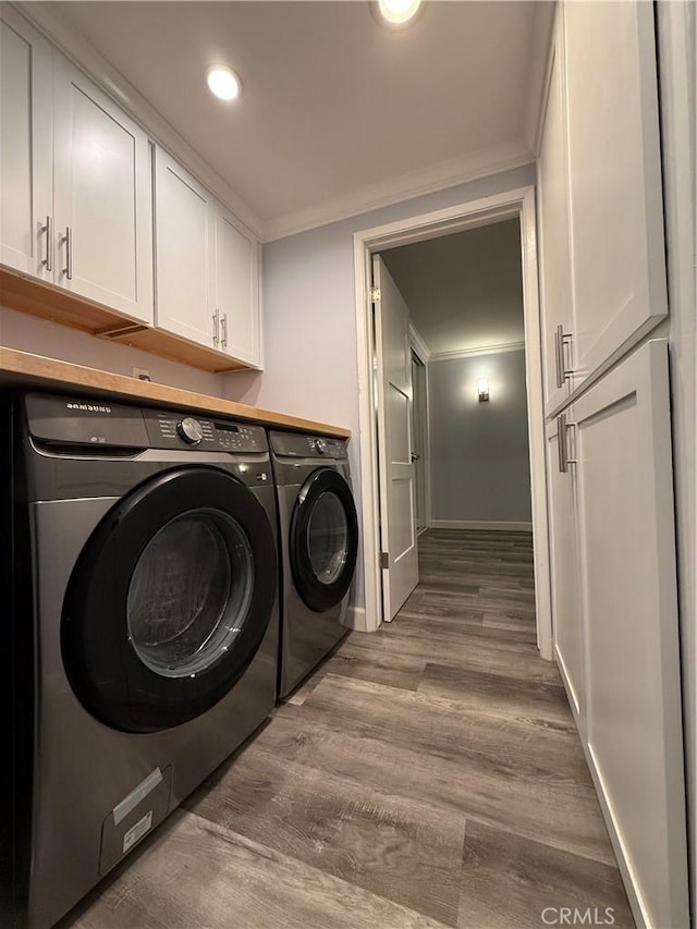 laundry area featuring washing machine and dryer, baseboards, ornamental molding, wood finished floors, and cabinet space