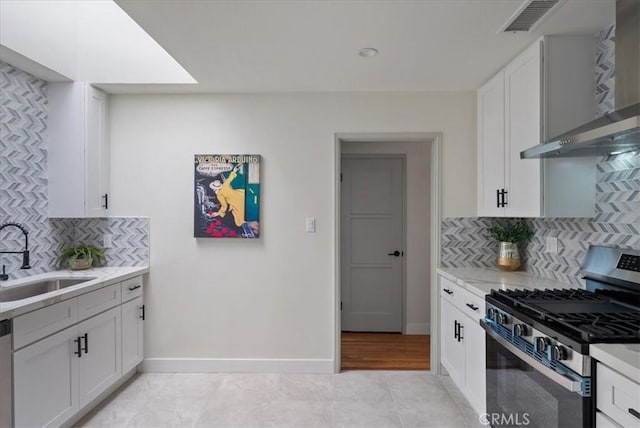kitchen featuring a sink, white cabinetry, backsplash, wall chimney range hood, and appliances with stainless steel finishes