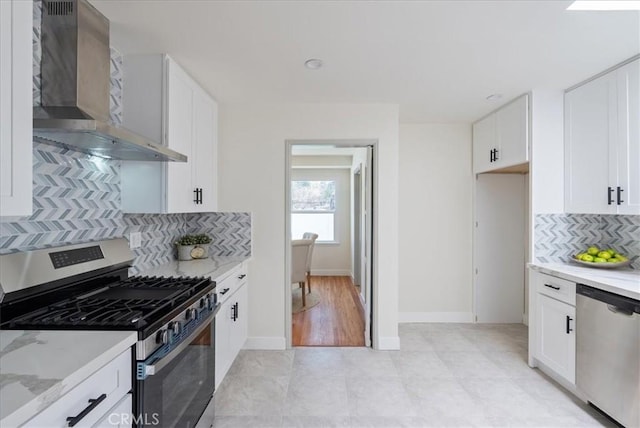 kitchen with white cabinetry, light stone countertops, wall chimney range hood, appliances with stainless steel finishes, and tasteful backsplash