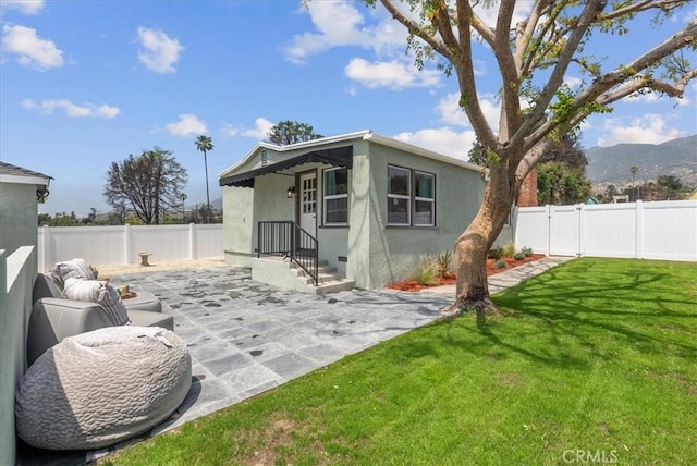 back of house with a patio area, a mountain view, stucco siding, a fenced backyard, and a lawn