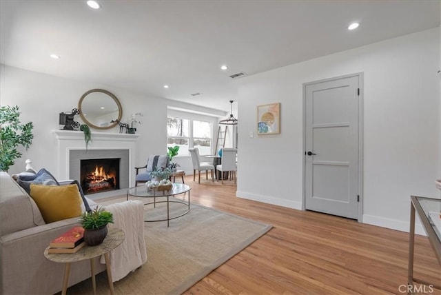 living room with a warm lit fireplace, recessed lighting, baseboards, light wood finished floors, and visible vents