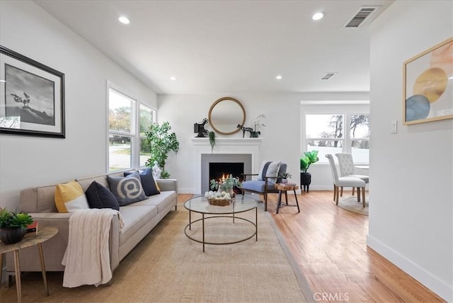 living room featuring a warm lit fireplace, light wood-style floors, recessed lighting, and visible vents